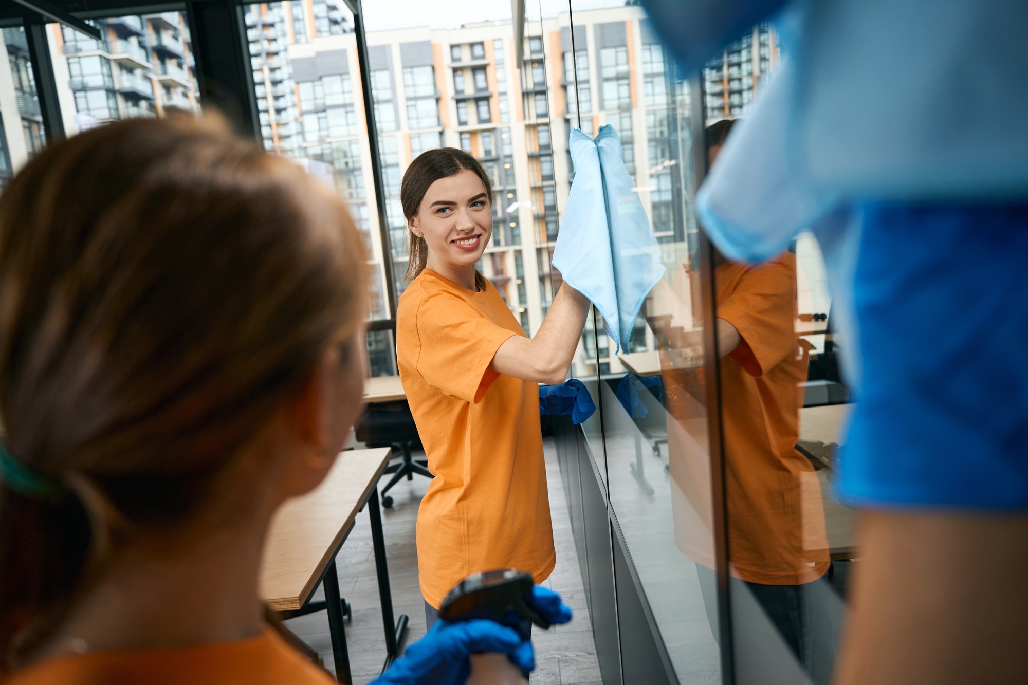 Young female employees cleaning company cleaning windows in acoworking space